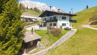 Traditionelles alpines Haus mit Bergblick, grüner Umgebung und einem kleinen Nebengebäude.