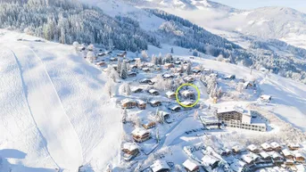 Winterliche Luftaufnahme eines Bergdorfes mit verschneiten Häusern und Skipisten.