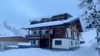 Traditionelles Holzhaus im alpinen Stil, umgeben von tiefem Schnee und winterlicher Landschaft.
