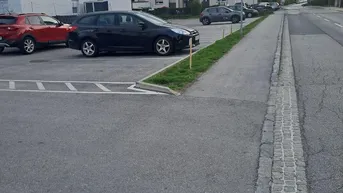 Parkplatz vor modernen Wohngebäuden mit weiteren Autos und einer Straße im Hintergrund unter bewölktem Himmel.