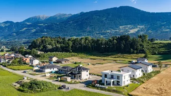 Luftaufnahme einer neuen Wohnsiedlung mit modernen Häusern und Bergblick in ländlicher Umgebung.