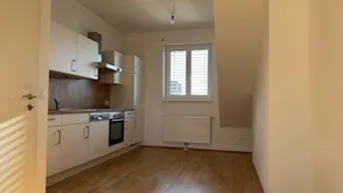 Helle Küche mit weißen Schränken, Holzarbeitsplatte und Dachschrägenfenster, ausgestattet mit grundlegenden Geräten.