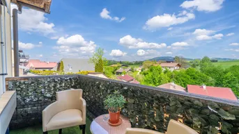 Gemütlicher Balkon mit Sitzgelegenheiten und weitem Blick über die grüne Landschaft unter blauem Himmel.
