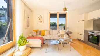 Helles Wohnzimmer mit beigem Sofa, Holzboden und integrierter Küchenzeile in offener Gestaltung.