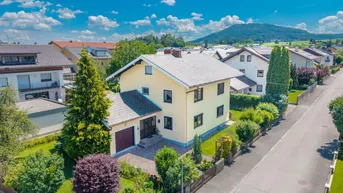 Drohnenaufnahme eines Einfamilienhauses mit gepflegtem Garten und Bergblick in einer Wohnsiedlung.