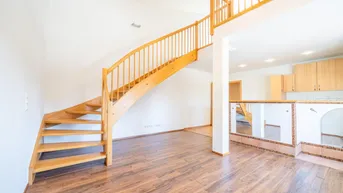 Helles Wohnzimmer mit Holztreppe und Laminatboden, offenem Übergang zur Küche.