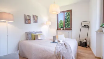 Helles Schlafzimmer mit Holzboden, gemütlichem Bett und Blick ins Grüne durch das Fenster.