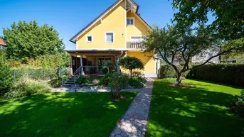 Rückansicht des Hauses mit überdachter Terrasse und einem gepflasterten Weg durch den Garten.
