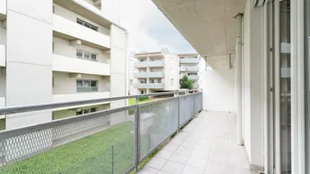 Geräumiger Balkon mit Fliesenboden und Metallgeländer, Blick auf Grünflächen und Nachbargebäude.