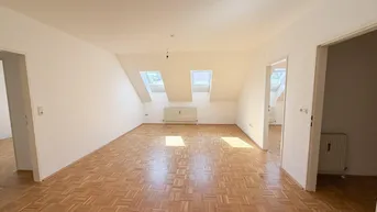 Helles Zimmer im Dachgeschoss mit Parkettboden, Dachschrägen und zwei Dachfenstern, die viel Licht hereinlassen.