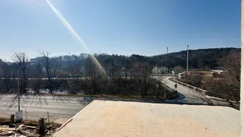 Weitblick über die Umgebung mit einer Straße, Bäumen und Hügeln unter blauem Himmel.