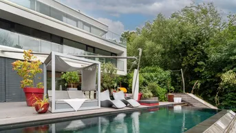 Moderne Villa mit luxuriösem Außenpool, Holzterrasse und stilvollen Lounge-Möbeln, umgeben von üppigem Grün.