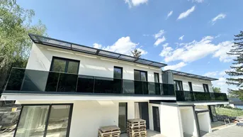Moderne Reihenhäuser im Bau mit großen Balkonen und Glasgeländern unter blauem Himmel.