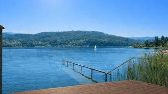 Holzsteg mit direktem Seezugang und Blick auf die umliegende Berglandschaft unter blauem Himmel.