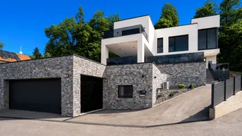 Moderne Architektur mit Steinfassade, Doppelgarage und gepflegter Auffahrt unter blauem Himmel.