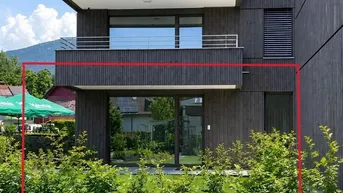 Moderne Erdgeschosswohnung mit dunkler Holzfassade und privatem Gartenanteil, umgeben von grünen Hecken.