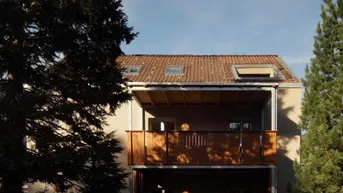 Modernes Gebäude mit Balkon, Terrasse und großem Gartenbereich unter blauem Himmel.