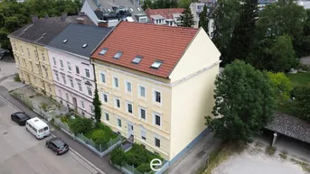 Luftaufnahme der Gebäudefassade mit gelbem Anstrich und rotem Ziegeldach in städtischer Umgebung.