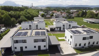 Luftaufnahme einer modernen Wohnsiedlung mit Reihenhäusern, Carports und Photovoltaikanlagen auf den Dächern.