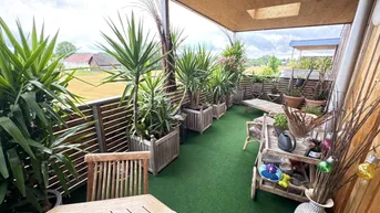 Geräumiger Balkon mit Kunstrasen, Holzmöbeln und vielen Pflanzen, ideal zum Entspannen im Freien.