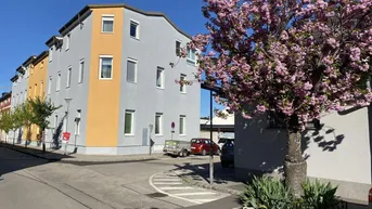 Mehrfamilienhaus mit moderner Fassade in Grau und Gelb, umgeben von blühenden Bäumen.