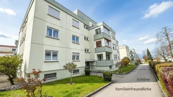 Mehrfamilienhaus mit heller Fassade und gepflegter Grünanlage unter blauem Himmel.
