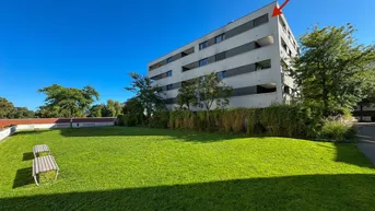 Modernes Mehrfamilienhaus mit gepflegter Rasenfläche und Bäumen unter blauem Himmel.