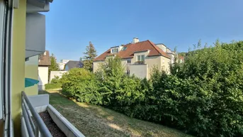 Blick vom Balkon auf die grüne Umgebung mit Hecken und einem gegenüberliegenden Gebäude.