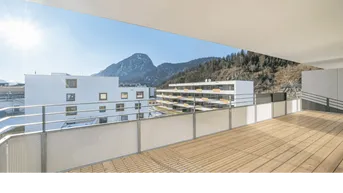Geräumiger Balkon mit Holzboden und weitem Blick auf die umliegende Berglandschaft und andere Gebäude.