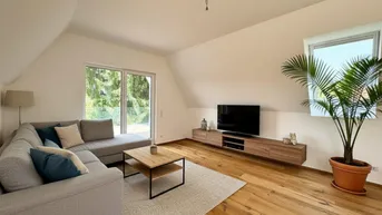 Gemütliches Wohnzimmer im Dachgeschoss mit Holzboden, Sofa und Blick ins Grüne.