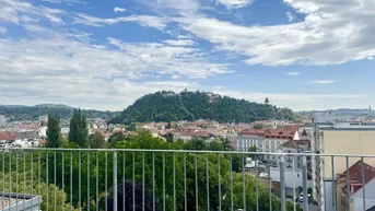 Panoramablick über die Stadt mit grünen Hügeln und historischer Architektur unter blauem Himmel.