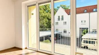 Heller Wohnraum mit Laminatboden und großen Fenstern, die einen Blick auf den Innenhof ermöglichen.