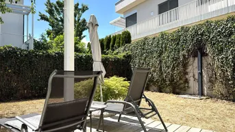 Entspannungsbereich im Garten mit Holzterrasse, Liegestühlen und grüner Hecke.