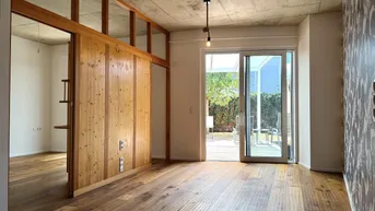 Heller Innenraum mit Holzboden, Sichtbetondecke und Zugang zu einer Terrasse.