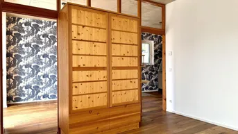 Geräumiger Flur mit großem Holzschrank, Holzboden und Zugang zu Zimmern mit gemusterter Tapete.
