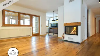 Geräumiger Wohnbereich mit Holzboden, Kamin und Zugang zu einem Wintergarten, der viel Licht hereinlässt.