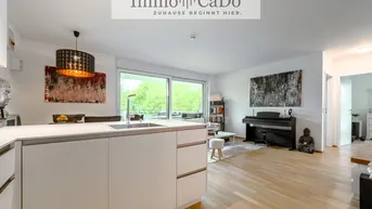 Heller offener Wohn- und Essbereich mit moderner Küche, Parkettboden und Zugang zum Balkon mit Grünblick.