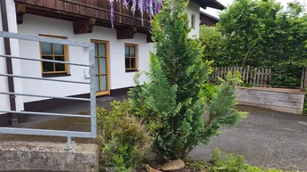 Außenansicht eines Hauses mit weißer Fassade, Holzelementen und grüner Bepflanzung im Vorgarten.