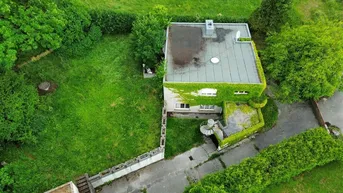 Luftaufnahme eines Hauses mit Flachdach, umgeben von viel Grün und einem Gartenbereich.
