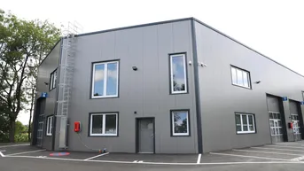 Modernes Gewerbegebäude mit grauer Fassade, weißen Fenstern und markierten Parkplätzen davor.