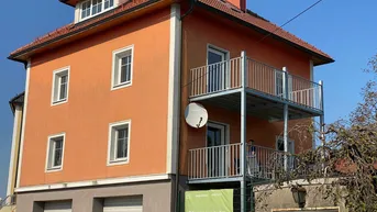 Wohnhaus mit oranger Fassade, Satteldach und zwei Balkonen, sowie Garagen im Erdgeschoss.