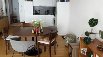Offener Wohn-Essbereich mit Holzboden und integrierter, moderner Küchenzeile in Weiß.