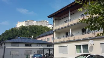 Gebäude mit Balkonen und Fernblick auf die Festung Hohensalzburg unter blauem Himmel.
