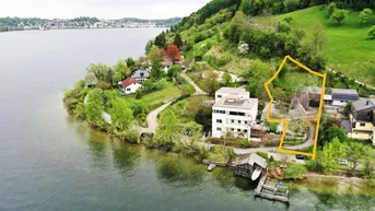 Luftaufnahme eines Anwesens am Seeufer mit umliegender Natur und Bergen im Hintergrund.