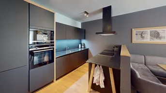 Moderne, offene Küche mit dunklen Schränken, integrierten Geräten und Holzboden.