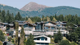 Moderne Gebäude in einer malerischen Berglandschaft mit üppigem Grün und klarem Himmel.
