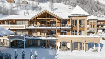 Luxuriöses Chalet-Gebäude in verschneiter Berglandschaft mit Holzfassade, Steinakzenten und Balkonen.
