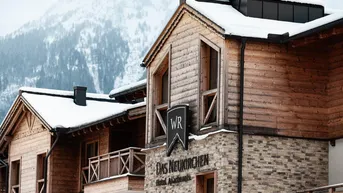 Modernes Gebäude im alpinen Stil mit Holzfassade und Steinverkleidung in verschneiter Berglandschaft.