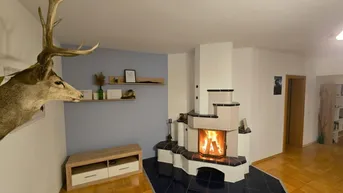 Gemütliches Wohnzimmer mit traditionellem Kachelofen, Holzboden und rustikaler Hirschgeweih-Dekoration.
