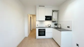 Moderne, helle Küche mit weißen Schränken, integrierten Geräten und hellem Laminatboden.